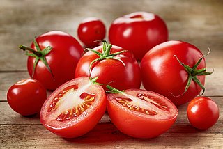 Mehrere Tomaten liegen auf einem Holzbrett. Davor liegt eine halbierte Tomate.